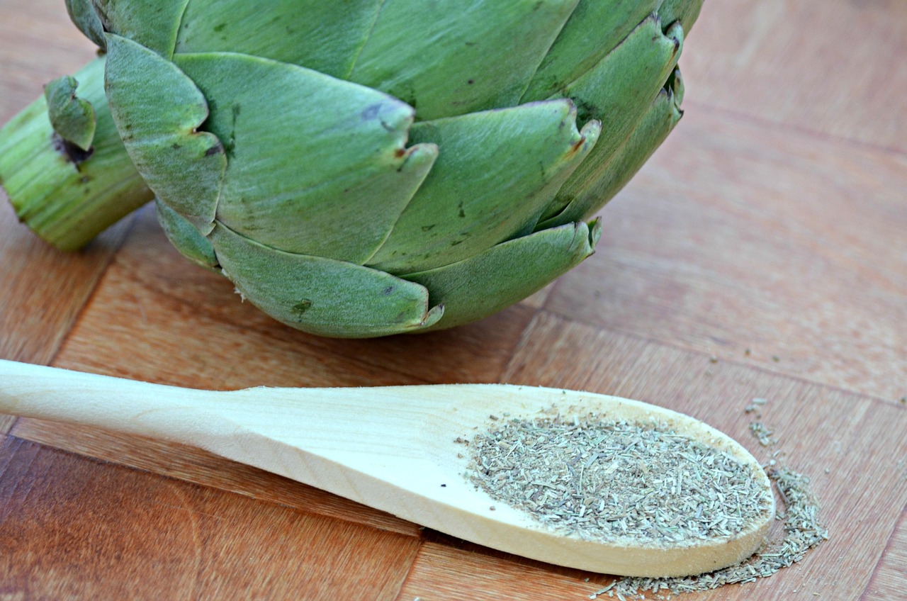green artichoke and wooden spoon with dried herbs
