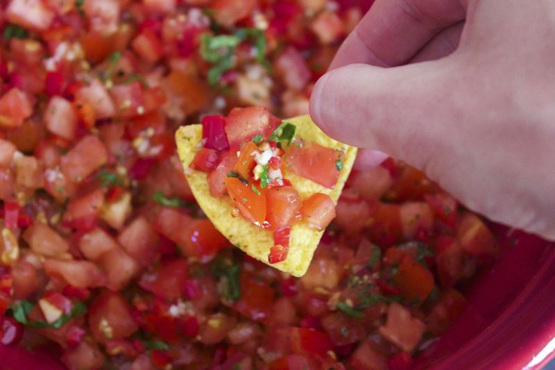 red tomato salsa with green herbs on a tortilla chip